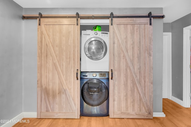 laundry area with stacked washer / dryer, hardwood / wood-style flooring, and a barn door