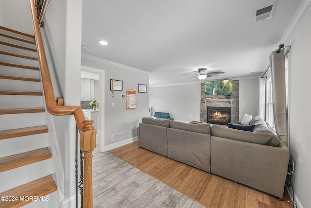 living room featuring light hardwood / wood-style flooring, ceiling fan, ornamental molding, and a stone fireplace