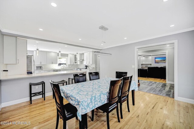 dining room featuring light wood-type flooring, ornamental molding, and sink