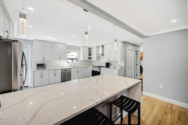 kitchen featuring light stone counters, wall chimney exhaust hood, pendant lighting, stainless steel appliances, and light hardwood / wood-style flooring