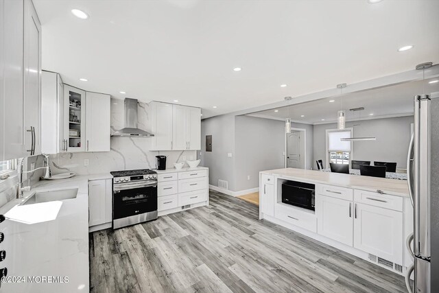 kitchen with decorative light fixtures, wall chimney range hood, white cabinetry, appliances with stainless steel finishes, and light stone countertops