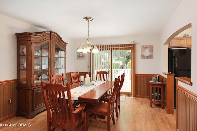 dining area with wood walls, light hardwood / wood-style flooring, and a notable chandelier