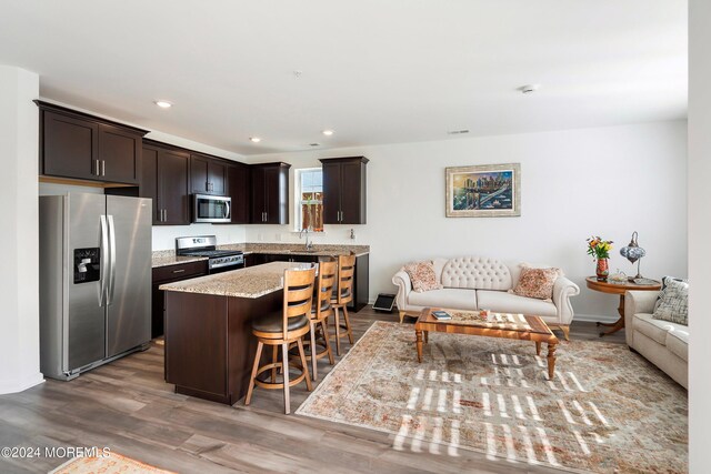 kitchen featuring dark brown cabinets, stainless steel appliances, a kitchen breakfast bar, a center island, and hardwood / wood-style floors