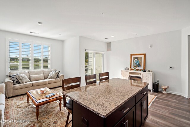 kitchen featuring light stone counters, dark brown cabinets, dark wood-type flooring, a kitchen breakfast bar, and a center island