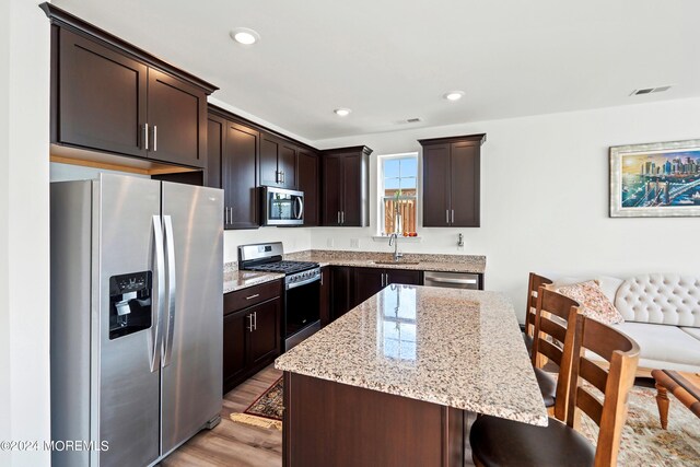 kitchen with dark brown cabinetry, sink, light hardwood / wood-style flooring, appliances with stainless steel finishes, and a center island