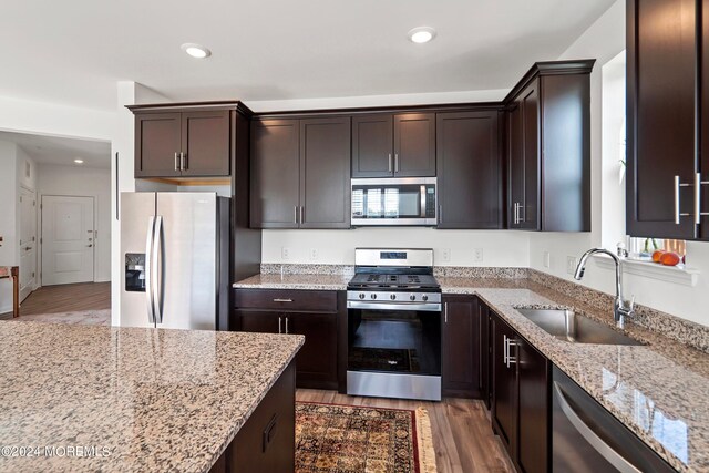 kitchen with light stone counters, dark brown cabinetry, sink, appliances with stainless steel finishes, and light hardwood / wood-style floors