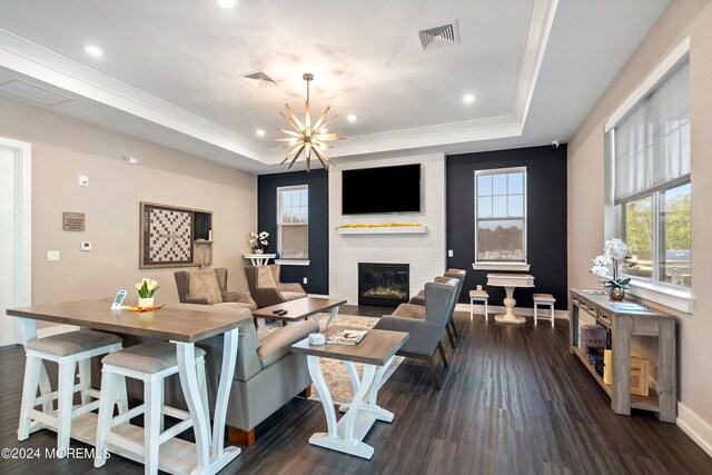 living room featuring a notable chandelier, a large fireplace, a tray ceiling, and dark hardwood / wood-style floors