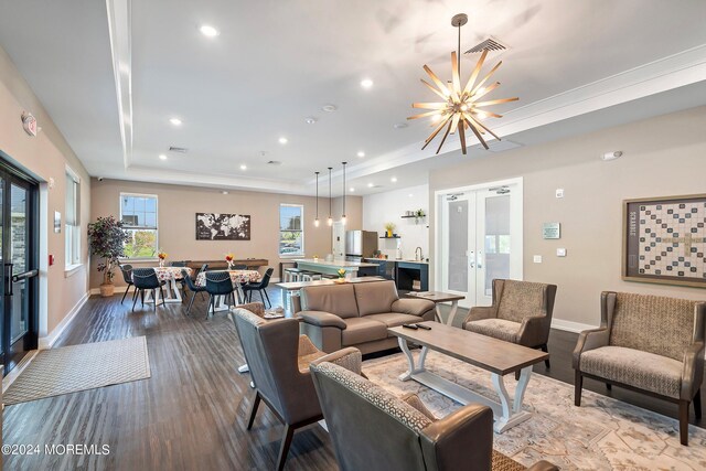 living room with light hardwood / wood-style floors, a tray ceiling, an inviting chandelier, and french doors