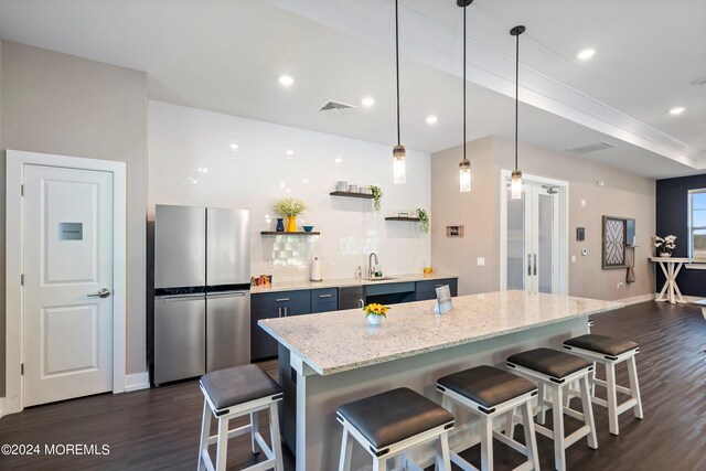 kitchen featuring a kitchen breakfast bar, stainless steel fridge, dark hardwood / wood-style flooring, decorative light fixtures, and sink