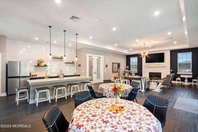 dining room featuring dark wood-type flooring, a raised ceiling, and a fireplace