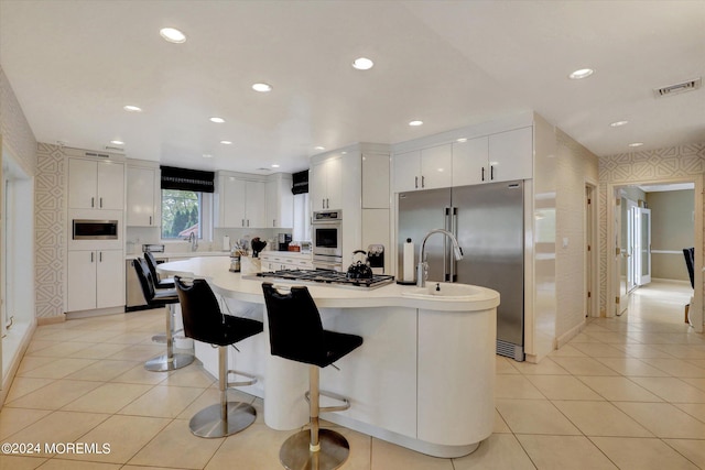 kitchen with light tile patterned flooring, a kitchen island, white cabinetry, stainless steel appliances, and a kitchen bar