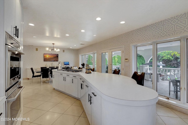 kitchen with white cabinets, hanging light fixtures, a kitchen island, a chandelier, and appliances with stainless steel finishes