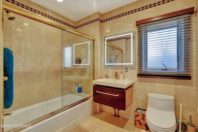 full bathroom featuring tile walls, shower / bath combination with glass door, vanity, and toilet