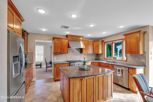 kitchen with a center island, sink, wall chimney exhaust hood, stainless steel appliances, and light tile patterned floors