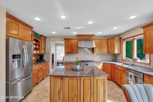 kitchen with appliances with stainless steel finishes, plenty of natural light, wall chimney range hood, and a center island