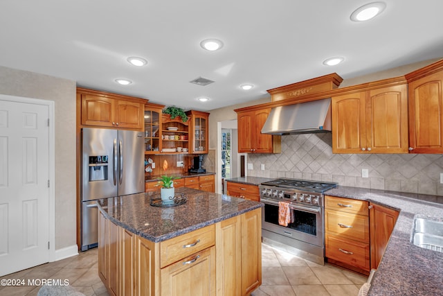 kitchen featuring a center island, tasteful backsplash, wall chimney exhaust hood, appliances with stainless steel finishes, and light tile patterned floors