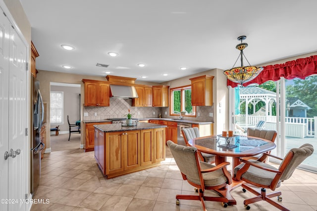 kitchen featuring pendant lighting, light tile patterned floors, wall chimney range hood, stainless steel appliances, and a center island