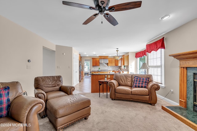 living room with ceiling fan with notable chandelier, a fireplace, and light carpet