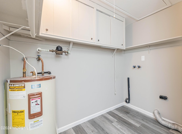laundry area featuring light wood finished floors, cabinet space, electric dryer hookup, water heater, and baseboards