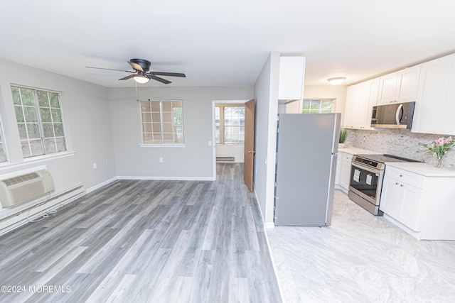 kitchen with appliances with stainless steel finishes, light countertops, baseboard heating, an AC wall unit, and a wealth of natural light