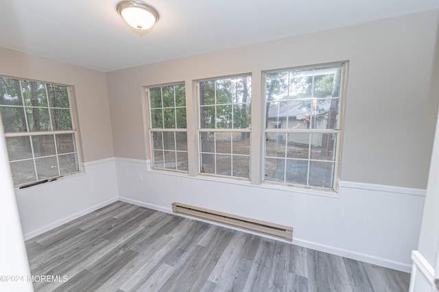 spare room featuring a wealth of natural light, baseboard heating, wainscoting, and wood finished floors