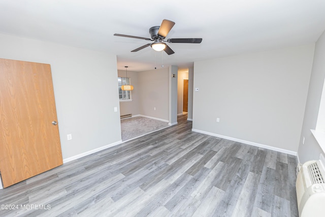 empty room with baseboard heating, baseboards, wood finished floors, and ceiling fan