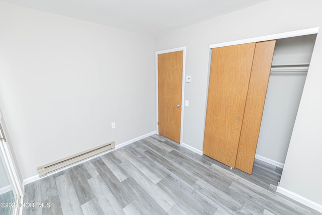 unfurnished bedroom with baseboards, a baseboard heating unit, a closet, and light wood finished floors