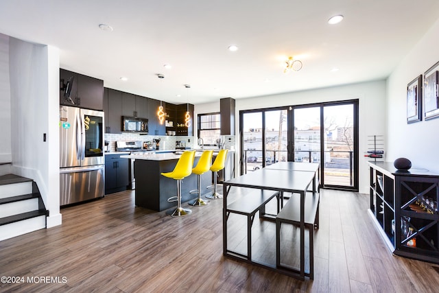 kitchen with pendant lighting, hardwood / wood-style floors, backsplash, appliances with stainless steel finishes, and a kitchen bar