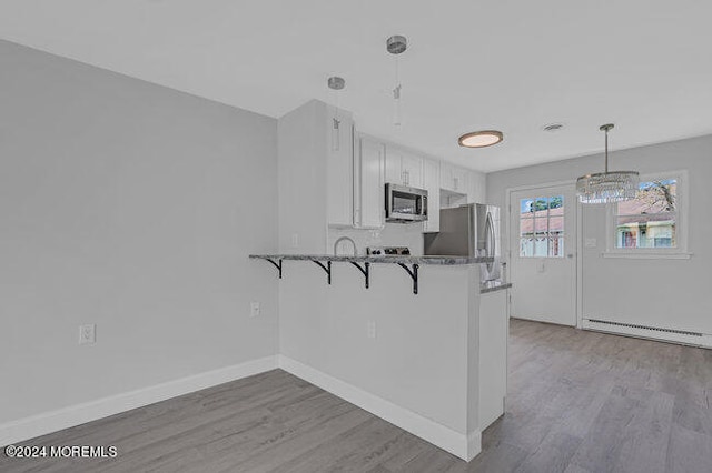 kitchen featuring white cabinetry, hanging light fixtures, a kitchen breakfast bar, stainless steel appliances, and baseboard heating