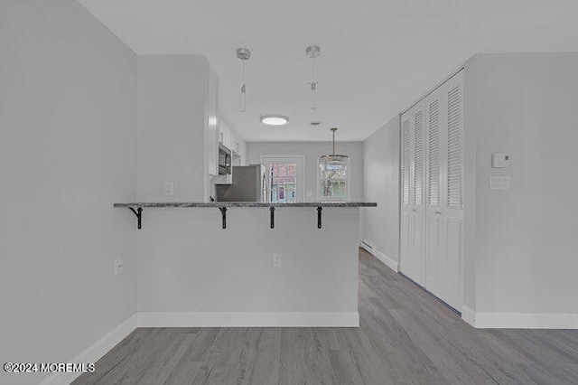 kitchen featuring white cabinets, kitchen peninsula, decorative light fixtures, a kitchen breakfast bar, and light wood-type flooring