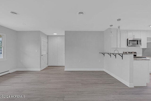 interior space with appliances with stainless steel finishes, white cabinets, kitchen peninsula, a breakfast bar area, and light hardwood / wood-style flooring