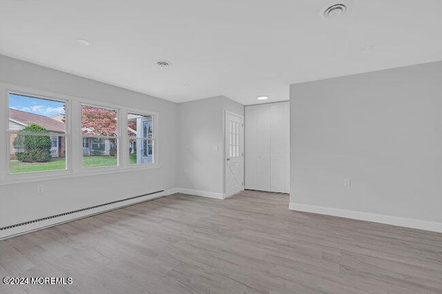 unfurnished room with a baseboard heating unit and light hardwood / wood-style floors