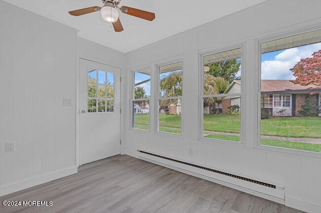 unfurnished sunroom featuring ceiling fan, plenty of natural light, and a baseboard heating unit