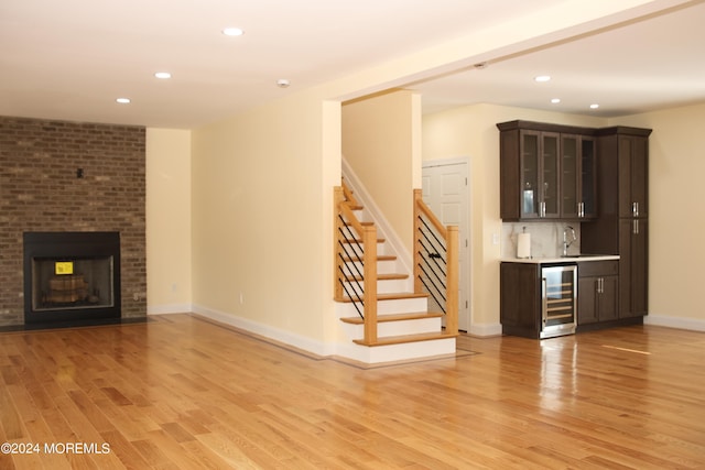 unfurnished living room featuring indoor wet bar, light hardwood / wood-style flooring, wine cooler, and a brick fireplace