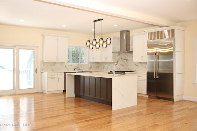 kitchen featuring light hardwood / wood-style floors, appliances with stainless steel finishes, hanging light fixtures, and wall chimney range hood