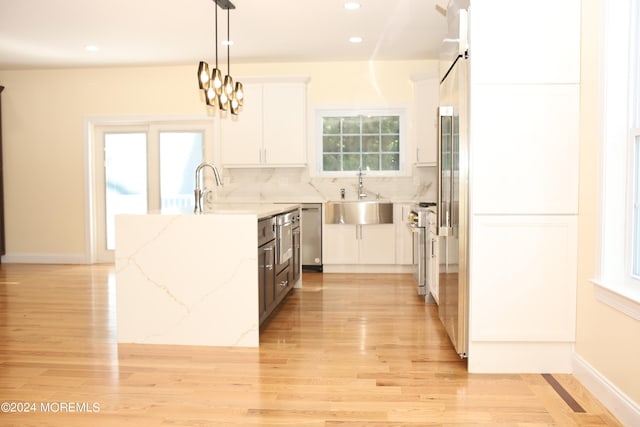 kitchen featuring hanging light fixtures, light hardwood / wood-style floors, white cabinetry, light stone countertops, and sink