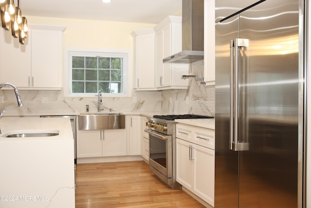 kitchen with light hardwood / wood-style floors, white cabinetry, wall chimney exhaust hood, premium appliances, and sink