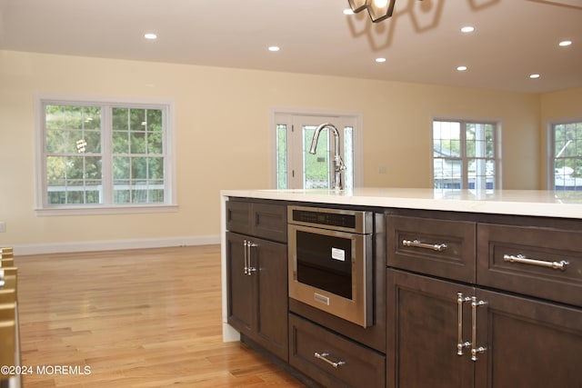 kitchen with a healthy amount of sunlight, dark brown cabinets, light hardwood / wood-style flooring, and stainless steel oven