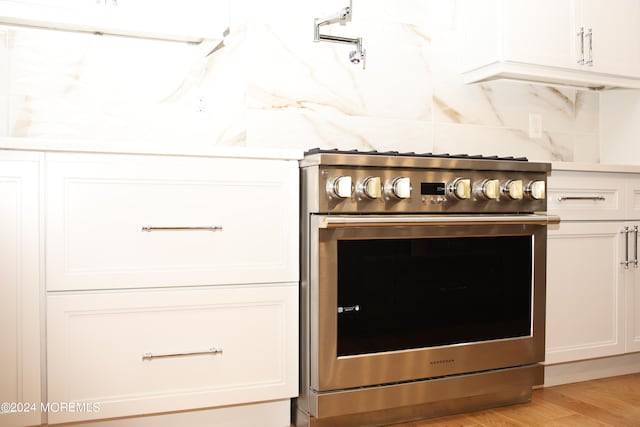 room details with high end stove, light hardwood / wood-style floors, white cabinetry, and tasteful backsplash