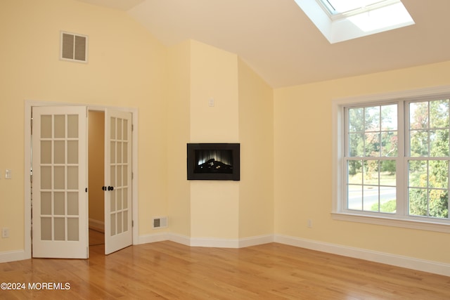 spare room with french doors, light wood-type flooring, a multi sided fireplace, and lofted ceiling with skylight