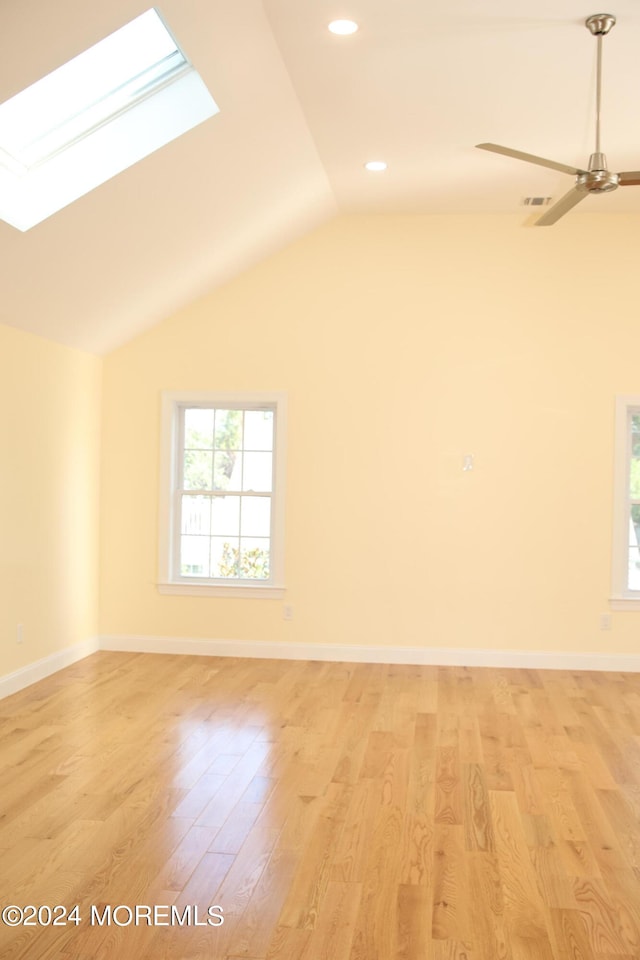 unfurnished room featuring ceiling fan, light wood-type flooring, and lofted ceiling with skylight