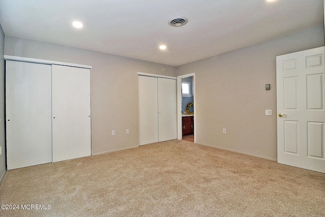 unfurnished bedroom featuring two closets, light colored carpet, and ensuite bath