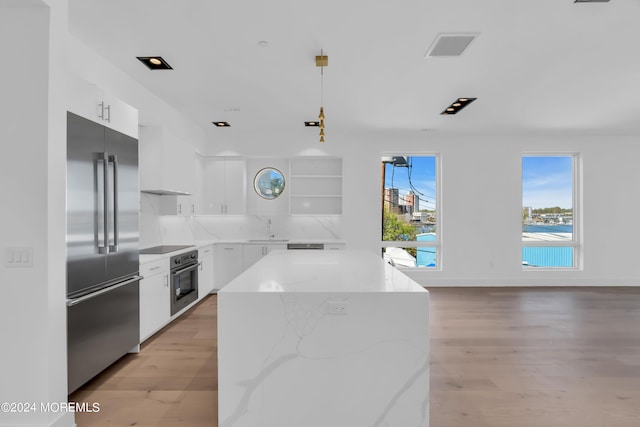 kitchen featuring light wood-type flooring, stainless steel appliances, pendant lighting, white cabinets, and a center island