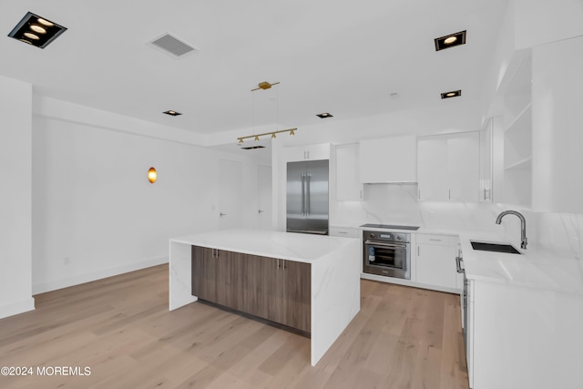 kitchen featuring appliances with stainless steel finishes, sink, a center island, light hardwood / wood-style floors, and white cabinetry