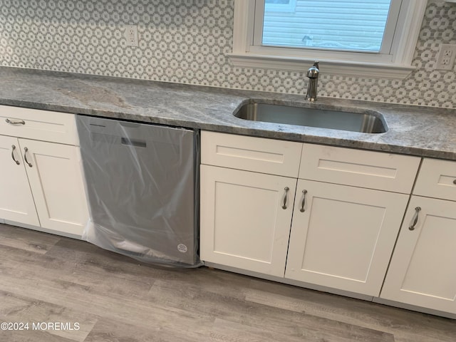 kitchen with light hardwood / wood-style floors, stainless steel dishwasher, sink, and white cabinets