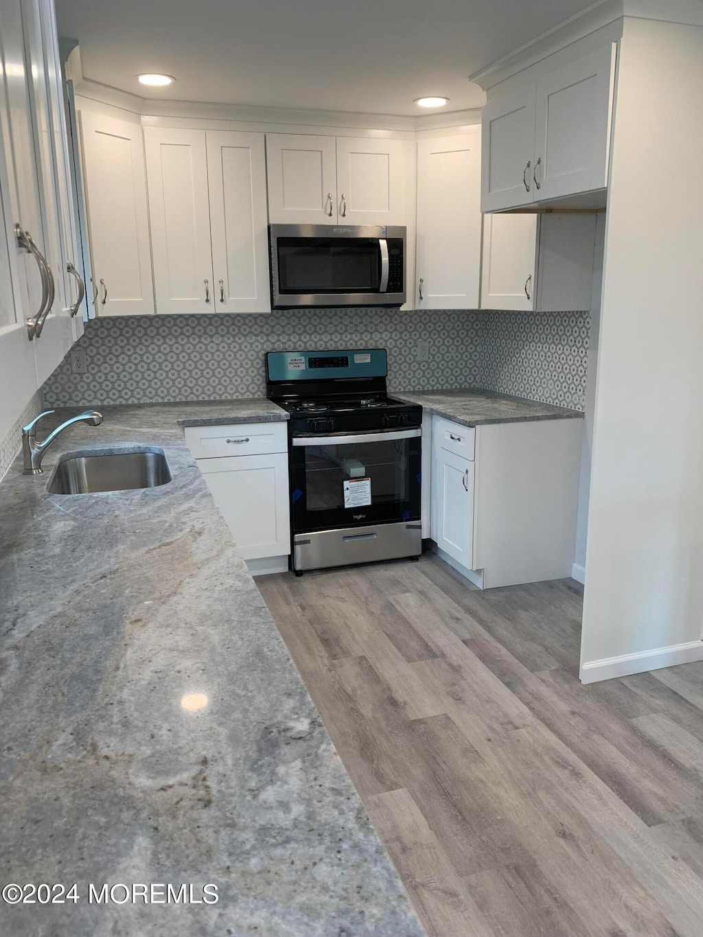 kitchen featuring a sink, white cabinets, light wood finished floors, stainless steel microwave, and gas stove