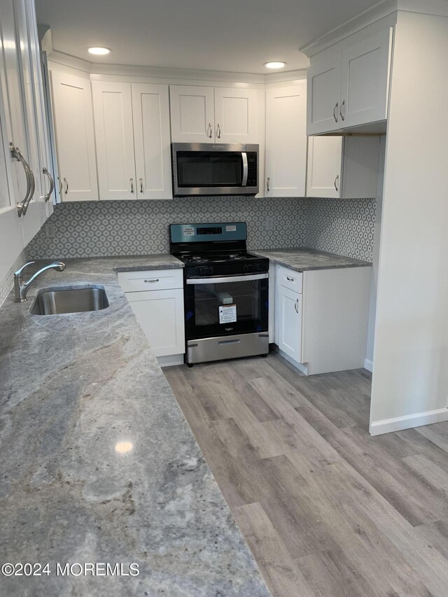 kitchen featuring a sink, white cabinets, light wood finished floors, stainless steel microwave, and gas stove