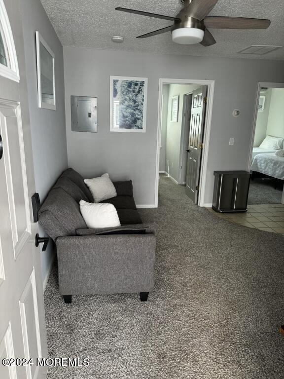 carpeted living room with ceiling fan, a textured ceiling, and electric panel