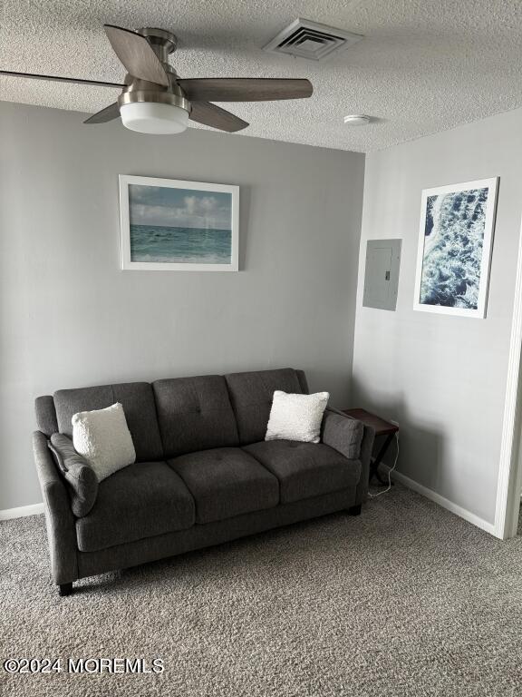 living room with ceiling fan, a textured ceiling, electric panel, and carpet flooring