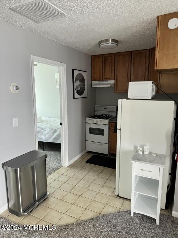 kitchen featuring a textured ceiling, white appliances, and light tile patterned floors